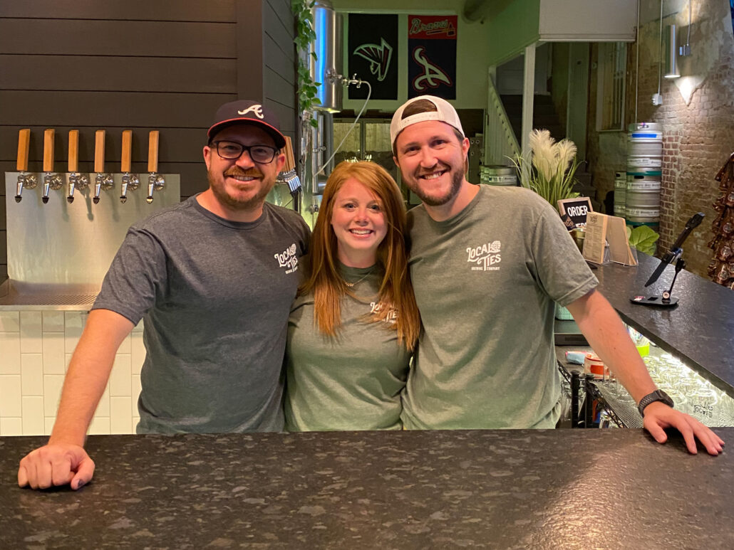 Alex, Tori, and Justin smiling behind the bar on opening night.